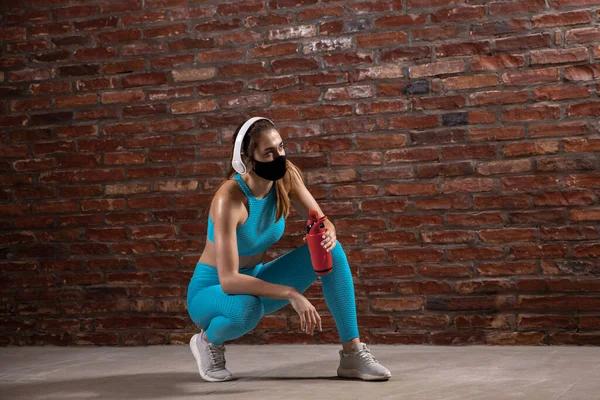 Treinamento atleta profissional feminino no fundo da parede de tijolo usando máscara facial. Desporto durante a quarentena — Fotografia de Stock