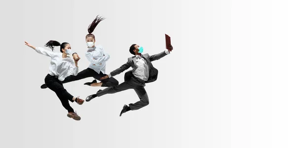 Glückliche Büroangestellte in Gesichtsmasken springen und tanzen in lässiger Kleidung oder Anzug isoliert auf Studiohintergrund. Kreative Collage. — Stockfoto