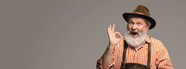 Happy senior man dressed in traditional Austrian or Bavarian costume gesturing isolated on grey studio background — Stock Photo, Image