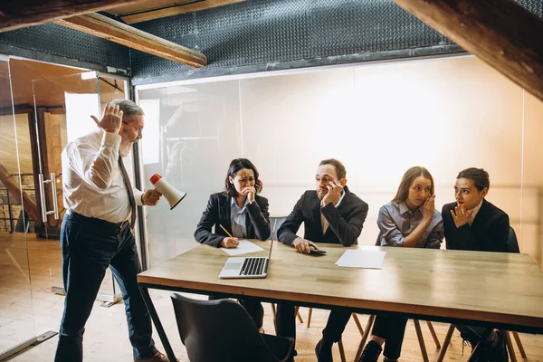 Wütender Chef mit Megafon schreit Mitarbeiter im Büro an, verängstigte und genervte Kollegen hören am Tisch zu — Stockfoto