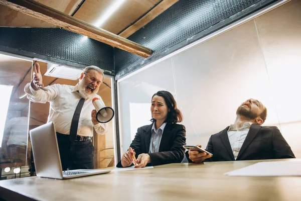 Patron en colère avec mégaphone criant sur les employés au bureau, collègues effrayés et agacés écoutant à la table — Photo