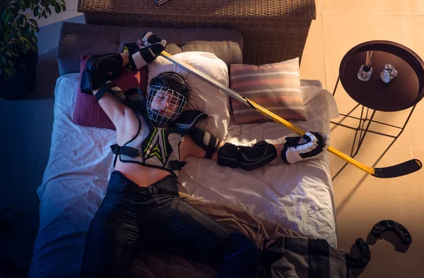 Pohled shora na mladého profesionálního hokejistu spícího v ložnici ve sportovním oblečení s vybavením — Stock fotografie