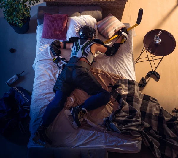 Widok z góry młodego profesjonalnego hokeisty śpiącego w swojej sypialni w odzieży sportowej ze sprzętem — Zdjęcie stockowe