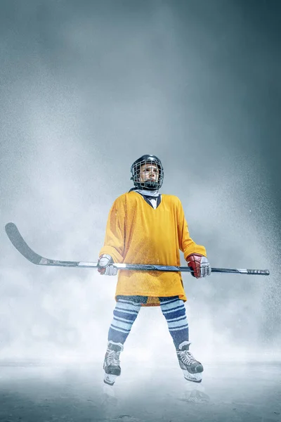 Pequeño jugador de hockey con el palo en la pista de hielo en humo. Sportsboy usando equipo y entrenamiento de casco en acción. — Foto de Stock