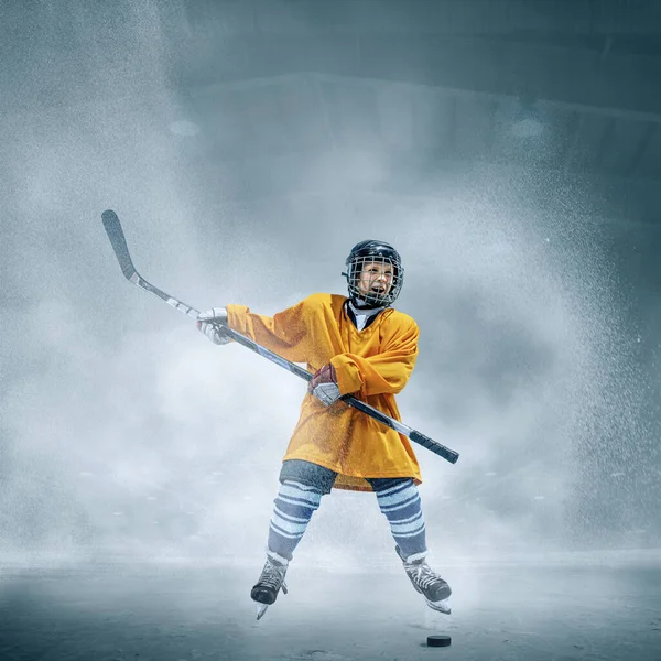 Pequeño jugador de hockey con el palo en la pista de hielo en humo. Sportsboy usando equipo y entrenamiento de casco en acción. — Foto de Stock