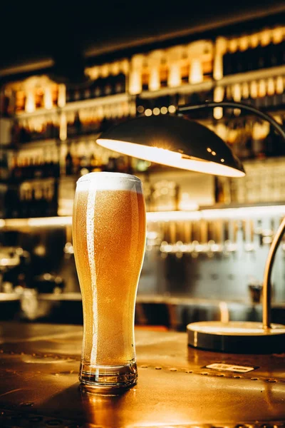 Vetro di birra lager su tavolo di legno in luce calda di bar — Foto Stock