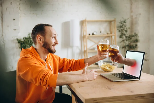Joven bebiendo cerveza durante la reunión con amigos en videollamada virtual. Distancia reunión en línea, chatear juntos en el ordenador portátil en casa. — Foto de Stock
