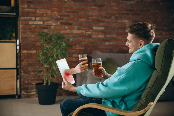 Joven bebiendo cerveza durante la reunión con amigos en videollamada virtual. Distancia reunión en línea, chatear juntos en la tableta en casa. — Foto de Stock