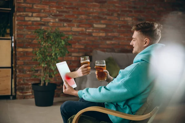 Joven bebiendo cerveza durante la reunión con amigos en videollamada virtual. Distancia reunión en línea, chatear juntos en la tableta en casa. — Foto de Stock