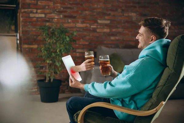 Joven bebiendo cerveza durante la reunión con amigos en videollamada virtual. Distancia reunión en línea, chatear juntos en la tableta en casa. — Foto de Stock