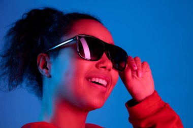 Afro-Amerikalı kadın portresi mavi stüdyo arka planında çok renkli neon ışıklarla izole edilmiş.