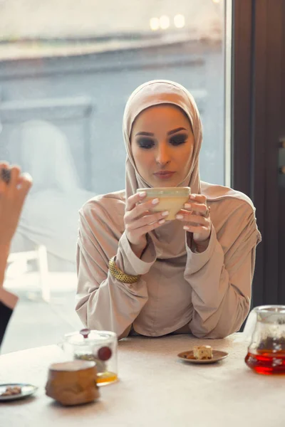 Beautiful arab woman meeting at cafe or restaurant with friend, spending time with cup of tea