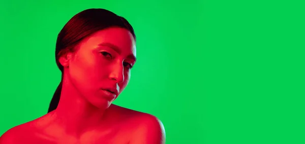 Beautiful east woman close up portrait isolated on green background in red neon light — Stock Photo, Image