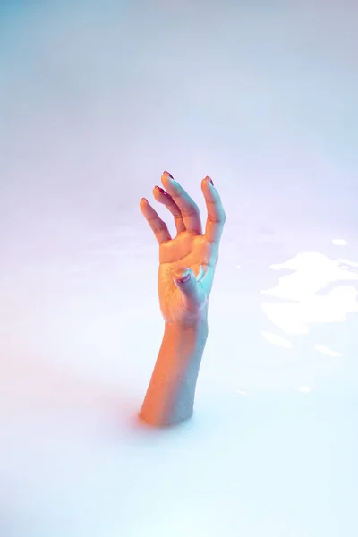 Close up female hand gesturing from the milk bath with soft glowing in neon light