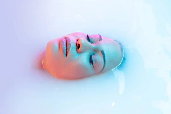 Закройте женское лицо в молочной ванне с мягким светящимся неоновым светом — стоковое фото