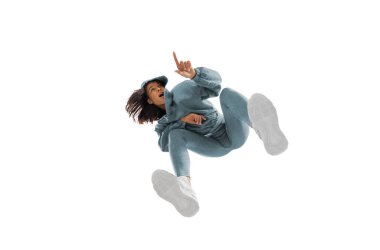 Modern sokak tarzı kıyafetli genç bir kadın beyaz arka planda izole edilmiş, alttan vurulmuş.