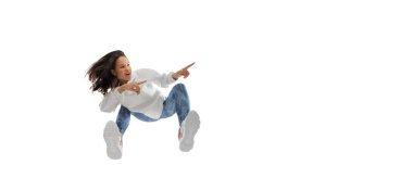 Modern sokak tarzı kıyafetli genç bir kadın beyaz arka planda izole edilmiş, alttan vurulmuş.