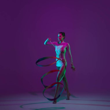 Genç bayan sporcu, ritmik jimnastik sanatçısı mor arka planda, neon ışıklı. Ekipmanlarla pratik yapan güzel bir kız. Gösteride zarafet.