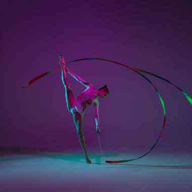 Genç bayan sporcu, ritmik jimnastik sanatçısı mor arka planda, neon ışıklı. Ekipmanlarla pratik yapan güzel bir kız. Gösteride zarafet.