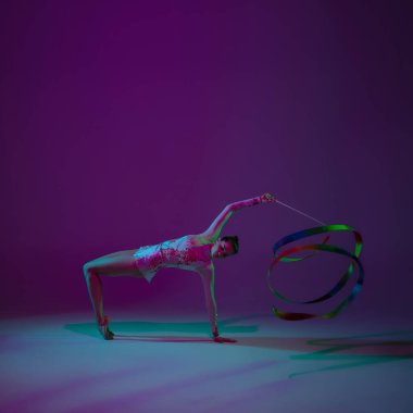 Genç bayan sporcu, ritmik jimnastik sanatçısı mor arka planda, neon ışıklı. Ekipmanlarla pratik yapan güzel bir kız. Gösteride zarafet.