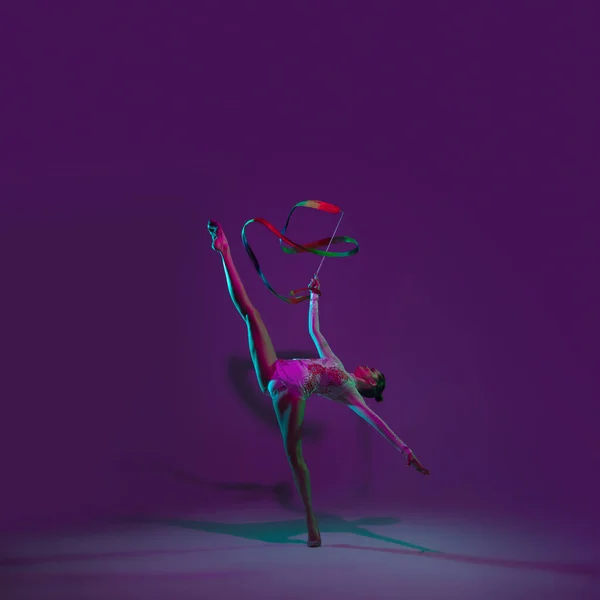 Jeune athlète féminine, artiste de gymnastique rythmique sur fond violet avec lumière au néon. Belle fille pratiquant avec l'équipement. Grace dans la performance. — Photo