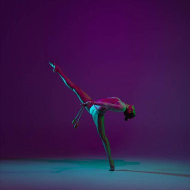 Genç bayan sporcu, ritmik jimnastik sanatçısı mor arka planda, neon ışıklı. Ekipmanlarla pratik yapan güzel bir kız. Gösteride zarafet.