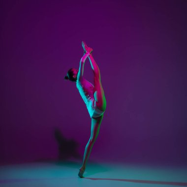 Genç bayan sporcu, ritmik jimnastik sanatçısı mor arka planda, neon ışıklı. Ekipmanlarla pratik yapan güzel bir kız. Gösteride zarafet.