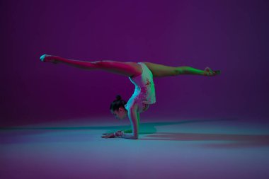 Genç bayan sporcu, ritmik jimnastik sanatçısı mor arka planda, neon ışıklı. Ekipmanlarla pratik yapan güzel bir kız. Gösteride zarafet.