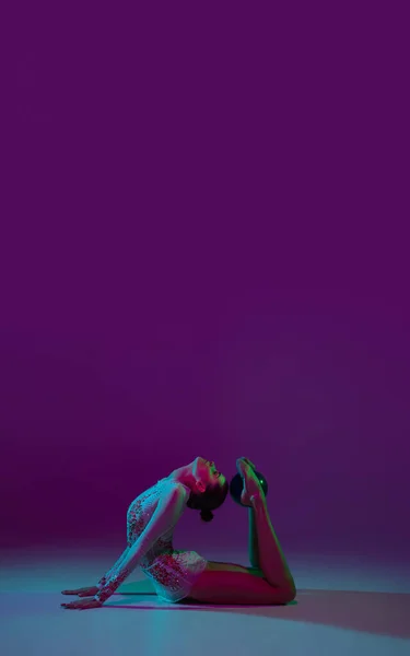 Young female athlete, rhythmic gymnastics artist on purple background with neon light. Beautiful girl practicing with equipment. Grace in performance. — Stock Photo, Image