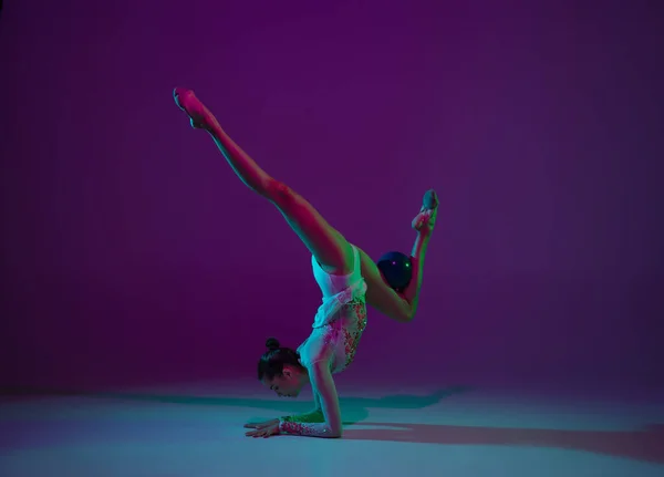 Jeune athlète féminine, artiste de gymnastique rythmique sur fond violet avec lumière au néon. Belle fille pratiquant avec l'équipement. Grace dans la performance. — Photo