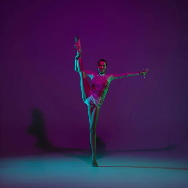 Jovem atleta feminina, artista de ginástica rítmica em fundo roxo com luz de néon. Menina bonita praticando com equipamento. Graça no desempenho. — Fotografia de Stock