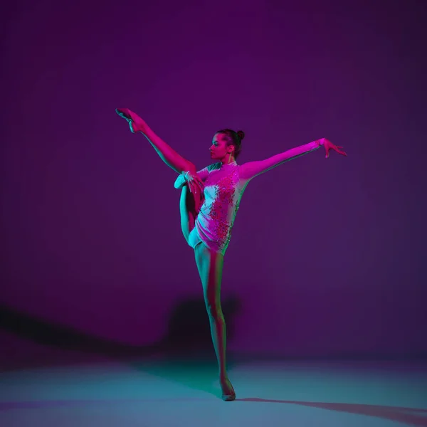 Jovem atleta feminina, artista de ginástica rítmica em fundo roxo com luz de néon. Menina bonita praticando com equipamento. Graça no desempenho. — Fotografia de Stock