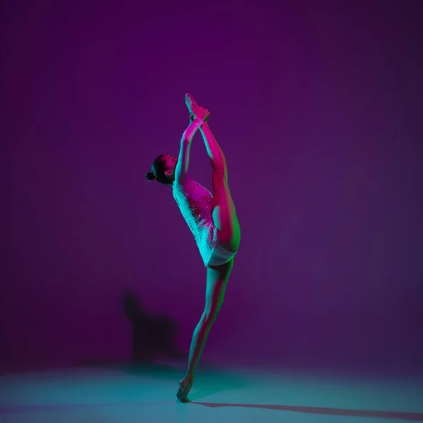 Giovane atleta femminile, ginnastica ritmica artista su sfondo viola con luce al neon. Bella ragazza che si esercita con l'attrezzatura. Grace in performance. — Foto Stock