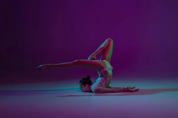 Jovem atleta feminina, artista de ginástica rítmica em fundo roxo com luz de néon. Menina bonita praticando com equipamento. Graça no desempenho. — Fotografia de Stock