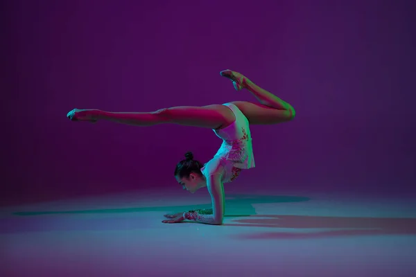 Jeune athlète féminine, artiste de gymnastique rythmique sur fond violet avec lumière au néon. Belle fille pratiquant avec l'équipement. Grace dans la performance. — Photo