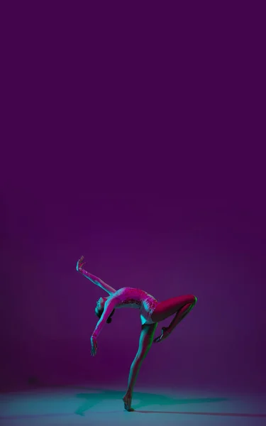 Genç bayan sporcu, ritmik jimnastik sanatçısı mor arka planda, neon ışıklı. Ekipmanlarla pratik yapan güzel bir kız. Gösteride zarafet. — Stok fotoğraf