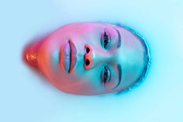 Красивое женское лицо в молочной ванне с мягким светящимся сине-розовым неоновым светом — стоковое фото