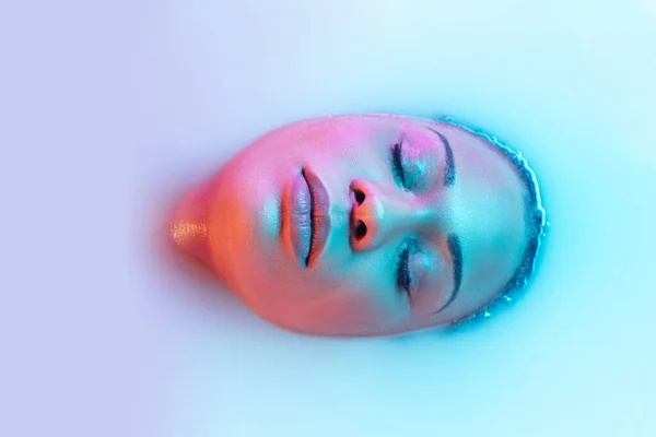 Beautiful female face in the milk bath with soft glowing in blue-pink neon light — Stock Photo, Image