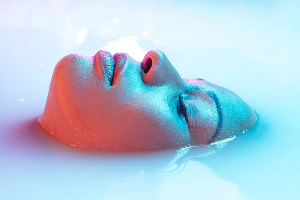 Красивое женское лицо в молочной ванне с мягким светящимся сине-розовым неоновым светом — стоковое фото