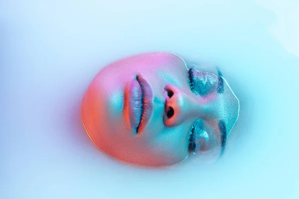 Bonito rosto feminino no banho de leite com suave brilhante em luz de néon azul-rosa — Fotografia de Stock
