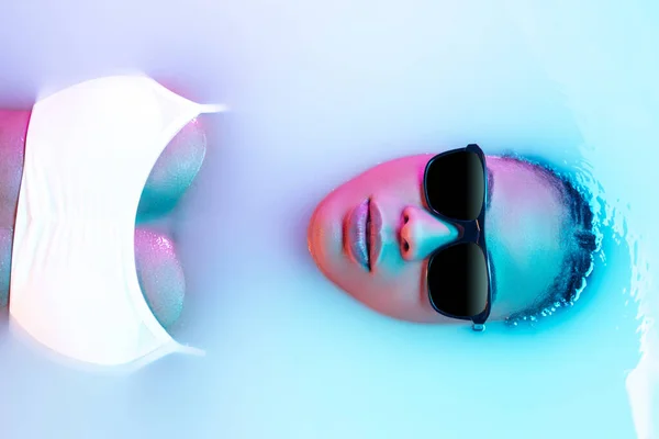 Beautiful female face in the milk bath with soft glowing in blue-pink neon light — Stock Photo, Image