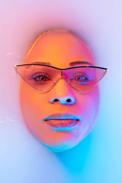 Beautiful female face in the milk bath with soft glowing in blue-pink neon light — Stock Photo, Image