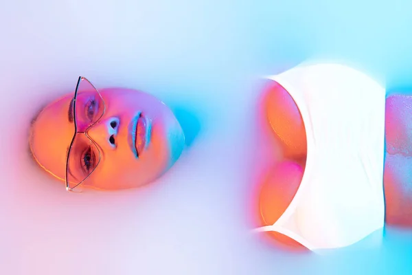 Bellissimo viso femminile nel bagno al latte con soffice incandescenza nella luce al neon blu-rosa — Foto Stock