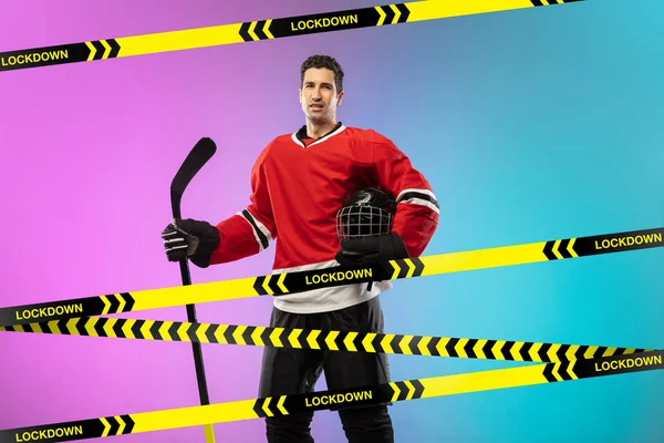 Männlicher Eishockeyspieler trägt Ausrüstung, Helm posiert auf Steigungshintergrund hinter Begrenzungsbändern mit Wort Lockdown — Stockfoto