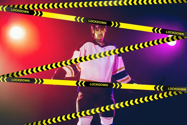 Männlicher Eishockeyspieler trägt Ausrüstung, Helm posiert auf Steigungshintergrund hinter Begrenzungsbändern mit Wort Lockdown — Stockfoto