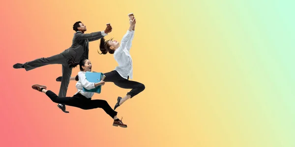 ハッピーオフィスの労働者がジャンプし、カジュアルな服やグラデーションネオン流体の背景に合わせて踊る。コピースペース付きフライヤー — ストック写真