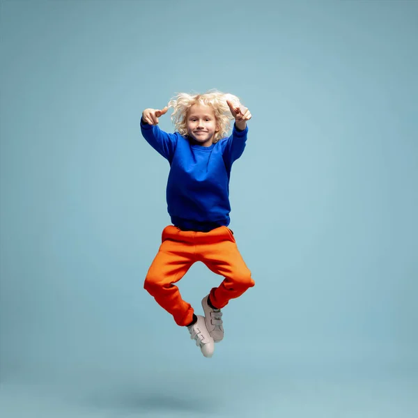 Happy curly boy isolated on blue studio background. Looks happy, cheerful, sincere. Copyspace. Childhood, education, emotions concept — Stock Photo, Image