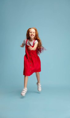 Happy redhair girl isolated on blue studio background. Looks happy, cheerful, sincere. Copyspace. Childhood, education, emotions concept clipart