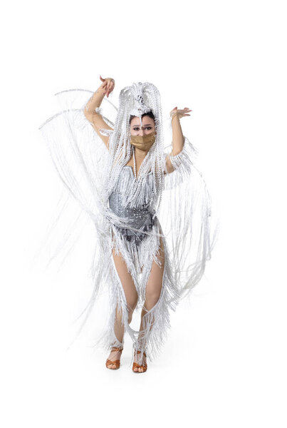 Beautiful young woman in carnival, stylish masquerade costume with feathers dancing on white studio background. Concept of holidays celebration, festive time, fashion