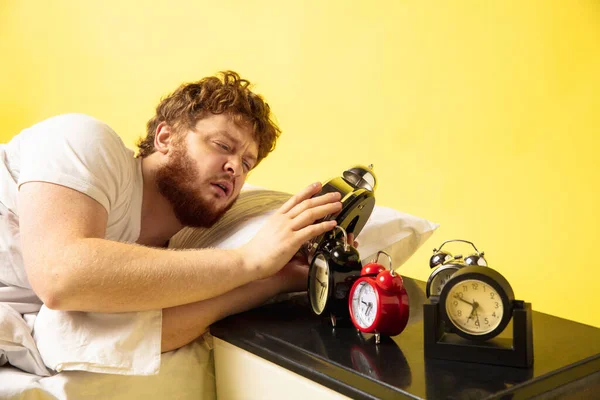 Man wakes up and hes mad at clock ringing, trying to switch it off, looks sleepy